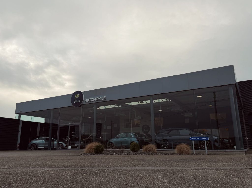 Façade extérieure vitrée du showroom EV Blue à Waremme avec véhicules électriques visibles